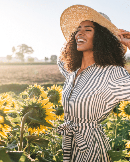 girl wearing stripe dress and hat smiling in sunflower field