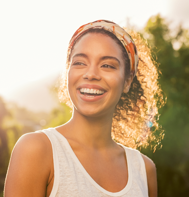 young lady with curly hair wearing white tank top and headband smiling